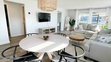 A modern living room with a round dining table, black metal chairs, a white sofa, and a large window.
