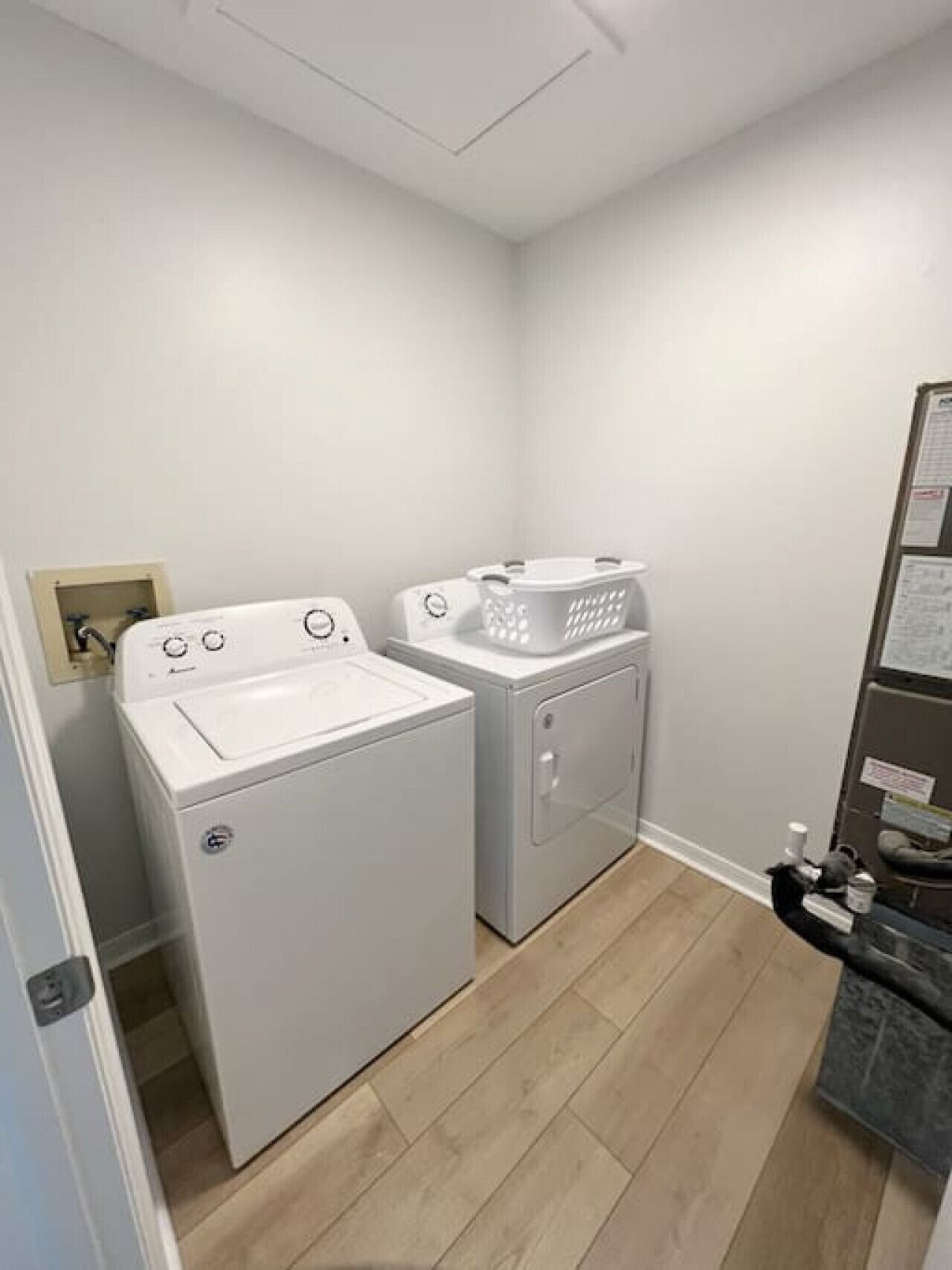 A laundry room with a front-loading washer and dryer, a drying rack, and a small shelf with cleaning supplies.