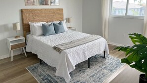 Un dormitorio con una cama grande, una mesita de noche, una planta y una ventana con cortinas.