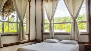 Quarto com cama, cortinas e vista para o verde lá fora.
