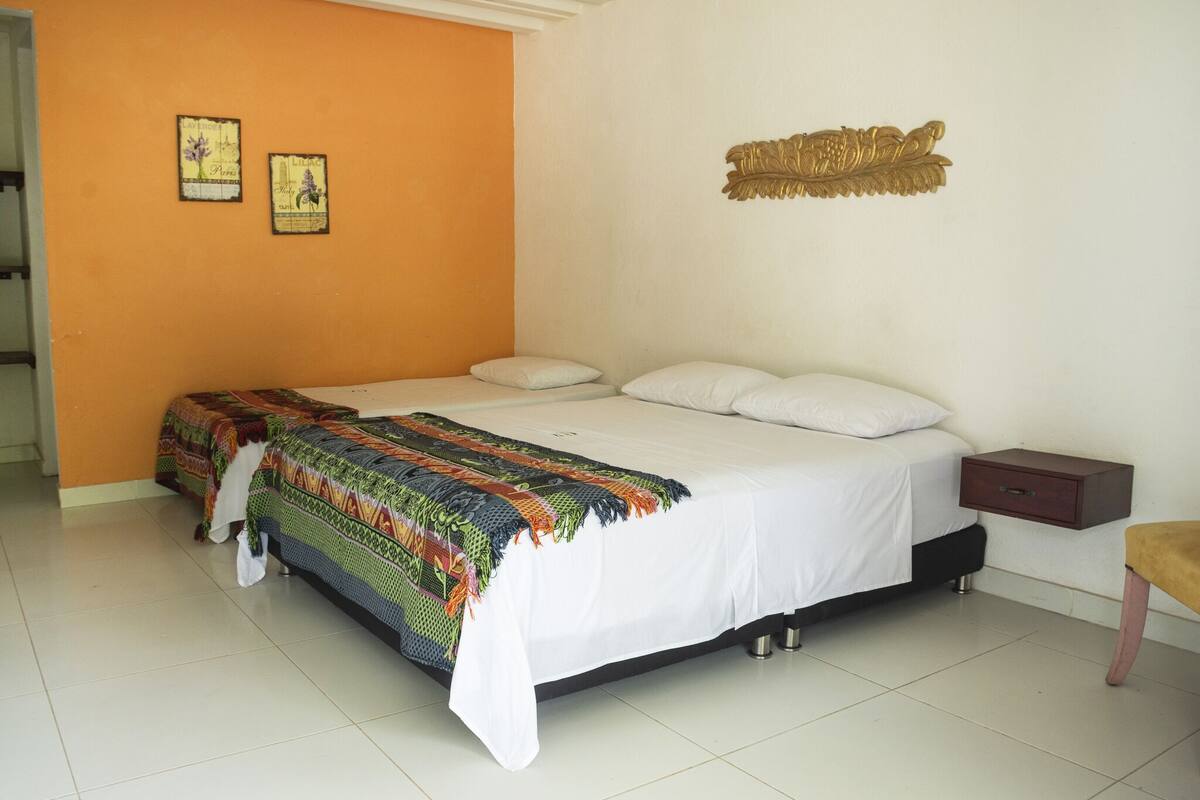 A bed with a colorful blanket, a nightstand, and a wall with two framed pictures.