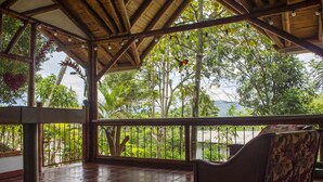 Uma área de estar coberta ao ar livre, com vista para vegetação exuberante e árvores.
