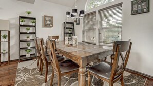 Ein Esszimmer mit Holztisch, Stühlen und einer Chandelüster. Regale mit Pflanzen und ein gerahmtes Bild sind an der Wand angebracht.