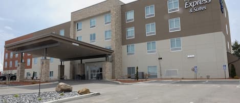 A Holiday Inn Express & Suites building with a covered entrance, stone pillars, and a parking lot.