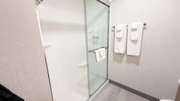 Un baño moderno con cabina de ducha de vidrio, inodoro y toallero con toallas.