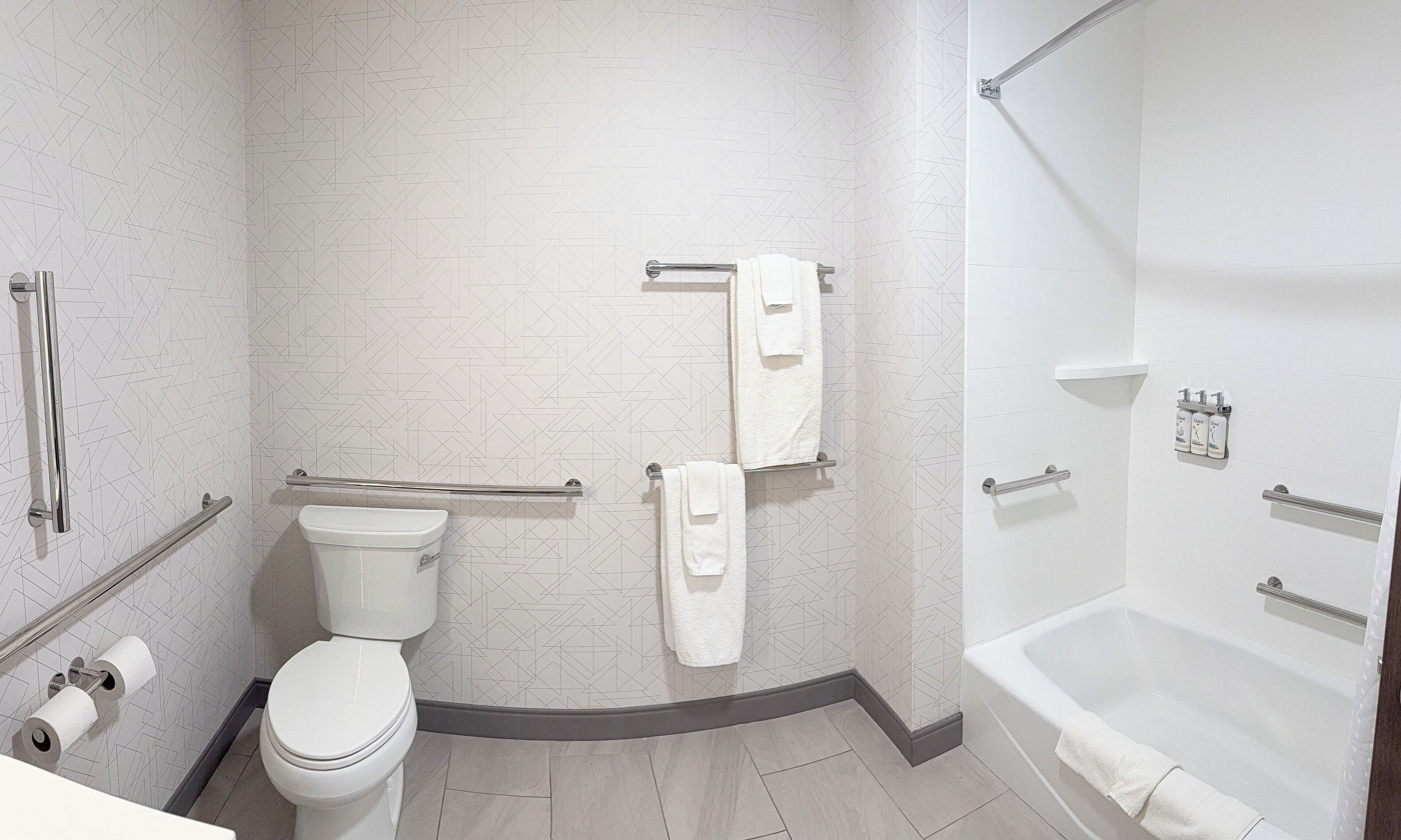 Une salle de bain moderne équipée de toilettes, d’une douche et d’une baignoire. On y trouve également des barres d’appui et un porte-serviettes.