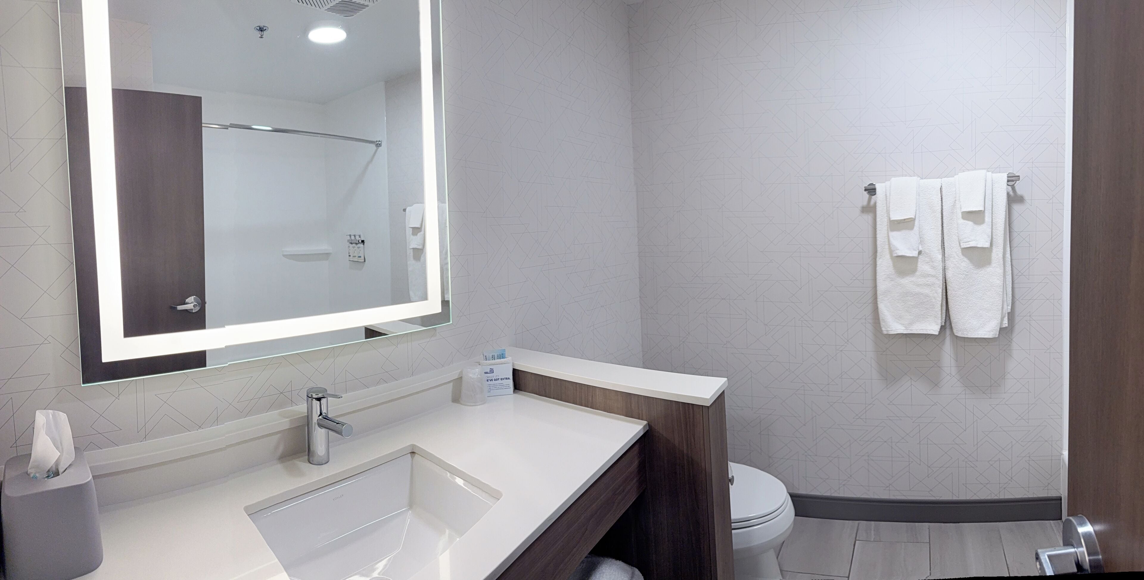 A modern bathroom with a large mirror, a sink, a toilet, and a towel rack.
