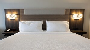A neatly made bed with white linens, two bedside tables with lamps, and a wall-mounted light fixture. - Holiday Inn Express & Suites Mansfield – Ontario by IHG (Mansfield)