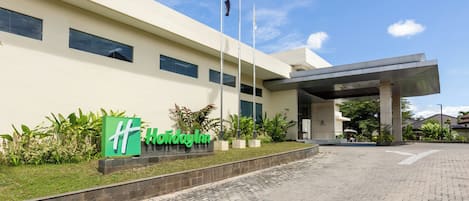A Holiday Inn hotel entrance with a paved driveway, a signboard, and a flagpole.