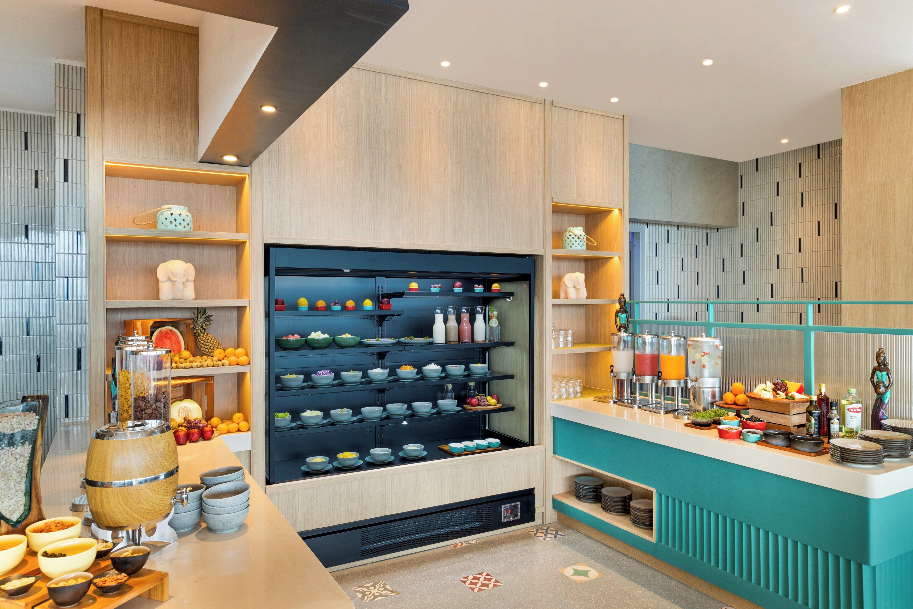 Una cocina moderna con armarios de madera, una isla central con cuencos y botellas, y una encimera color turquesa con diversos alimentos y bebidas.