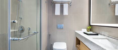 A modern bathroom with a glass shower enclosure, a white toilet, a towel rack with folded towels, and a countertop with a sink and a mirror.