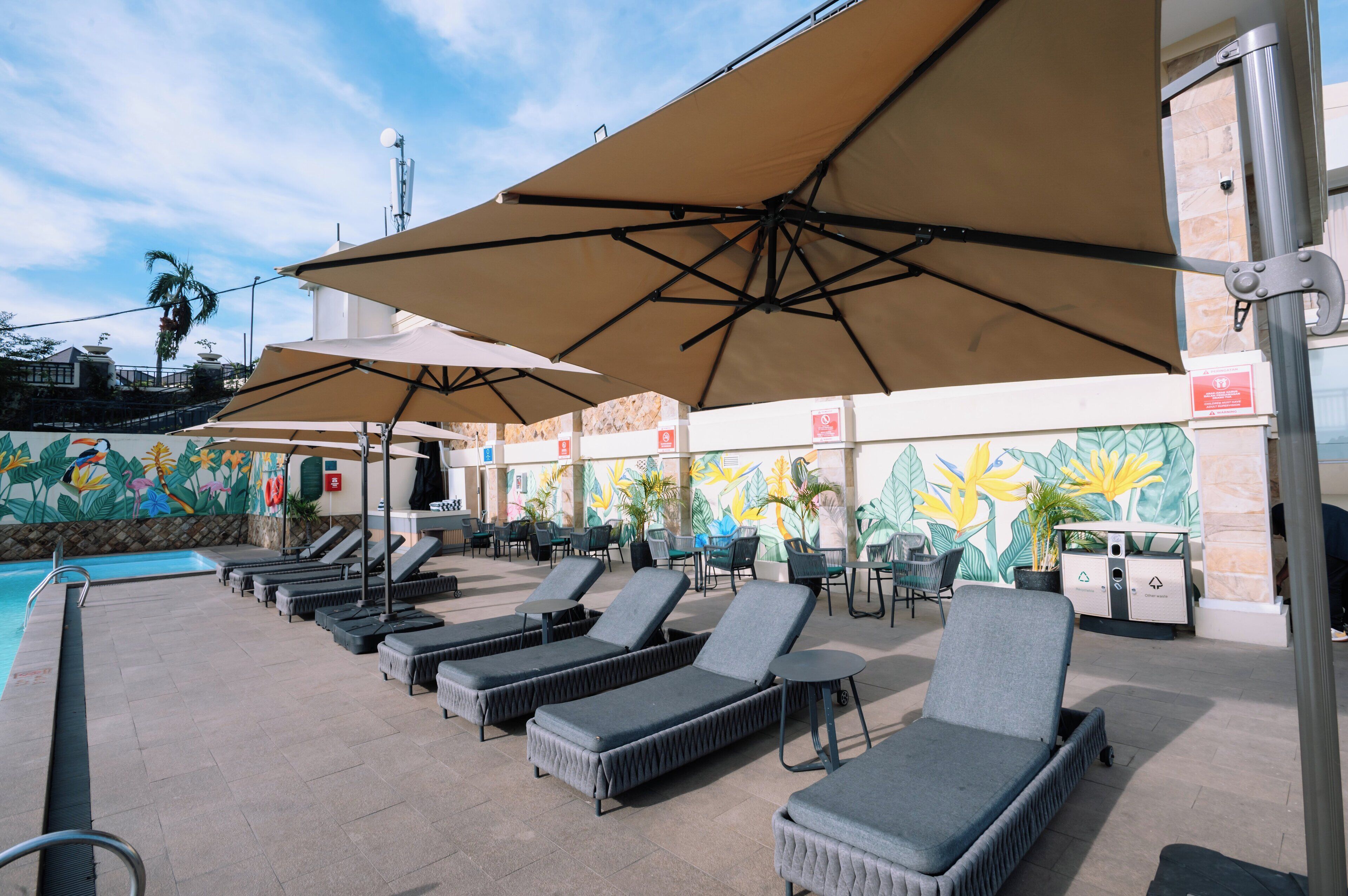 Een zwembadgedeelte met ligbedden en parasols, een muurschildering en een afvalstation.