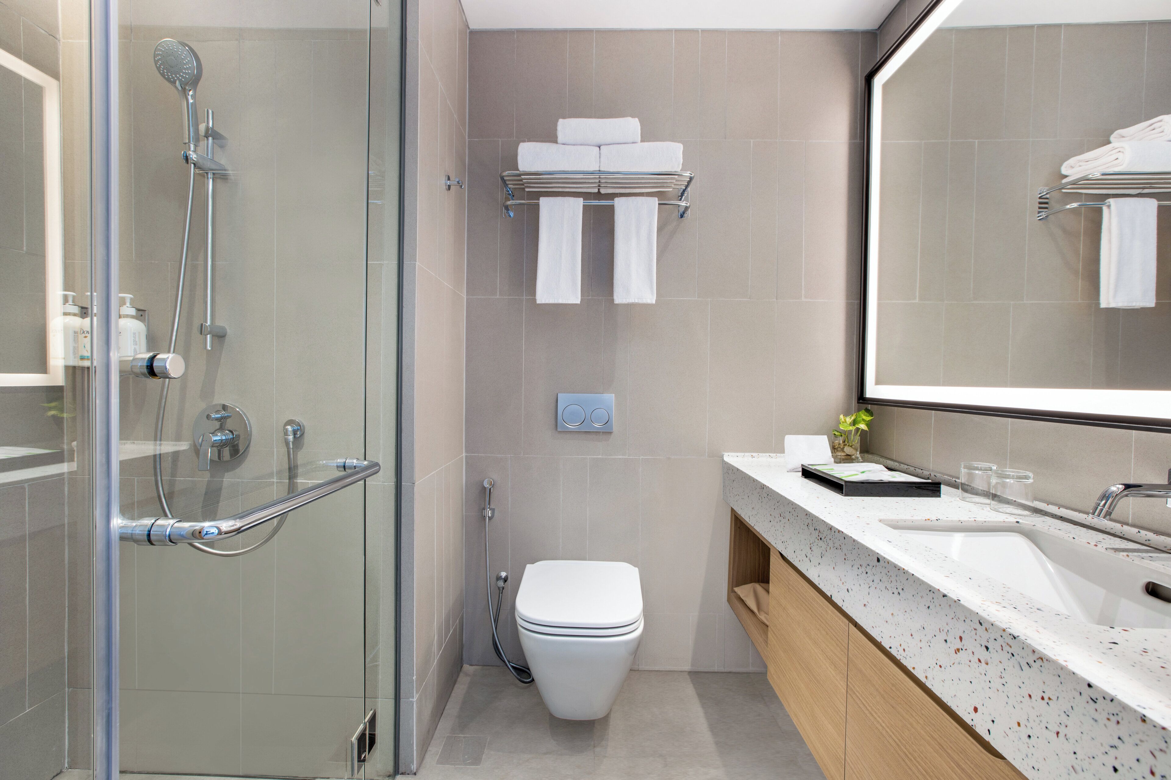 Un baño moderno con ducha de vidrio, inodoro, lavamanos con espejo y toallero.