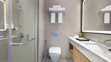 Un baño moderno con ducha de vidrio, inodoro, lavamanos con espejo y toallero.