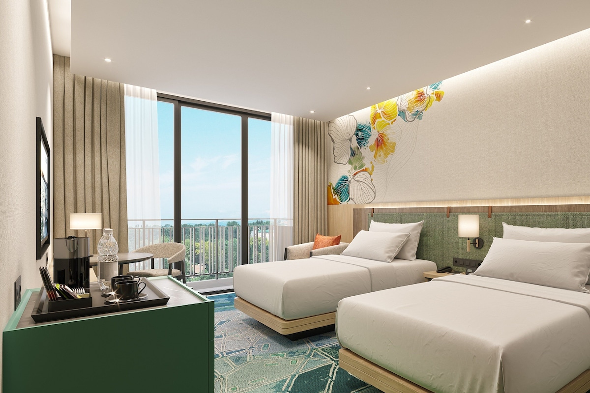 A hotel room with two beds, a desk with a lamp, a view of the cityscape, and a decorative wall piece.