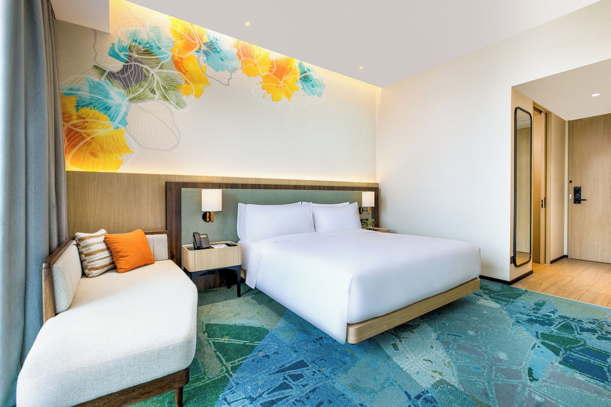 A hotel room with a bed, a sofa, a nightstand, a wall-mounted lamp, and a door.