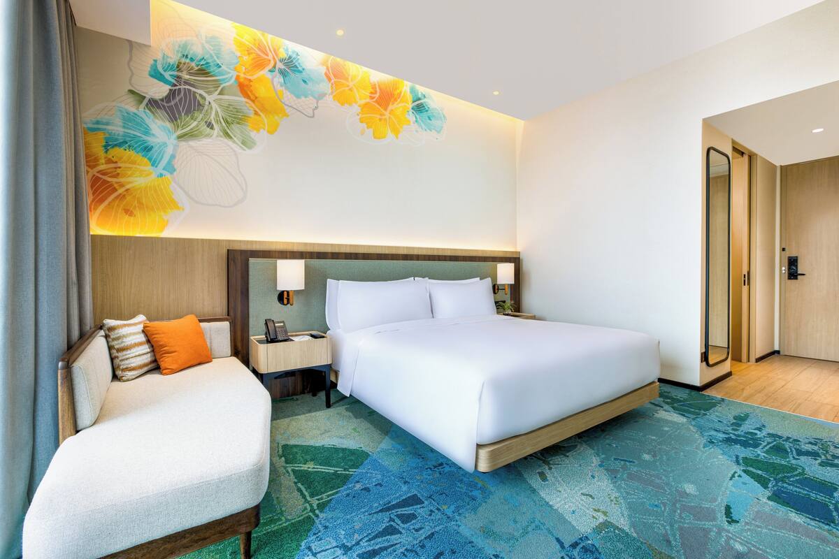 A hotel room with a large bed, a sofa, a nightstand, and a wall-mounted lamp.