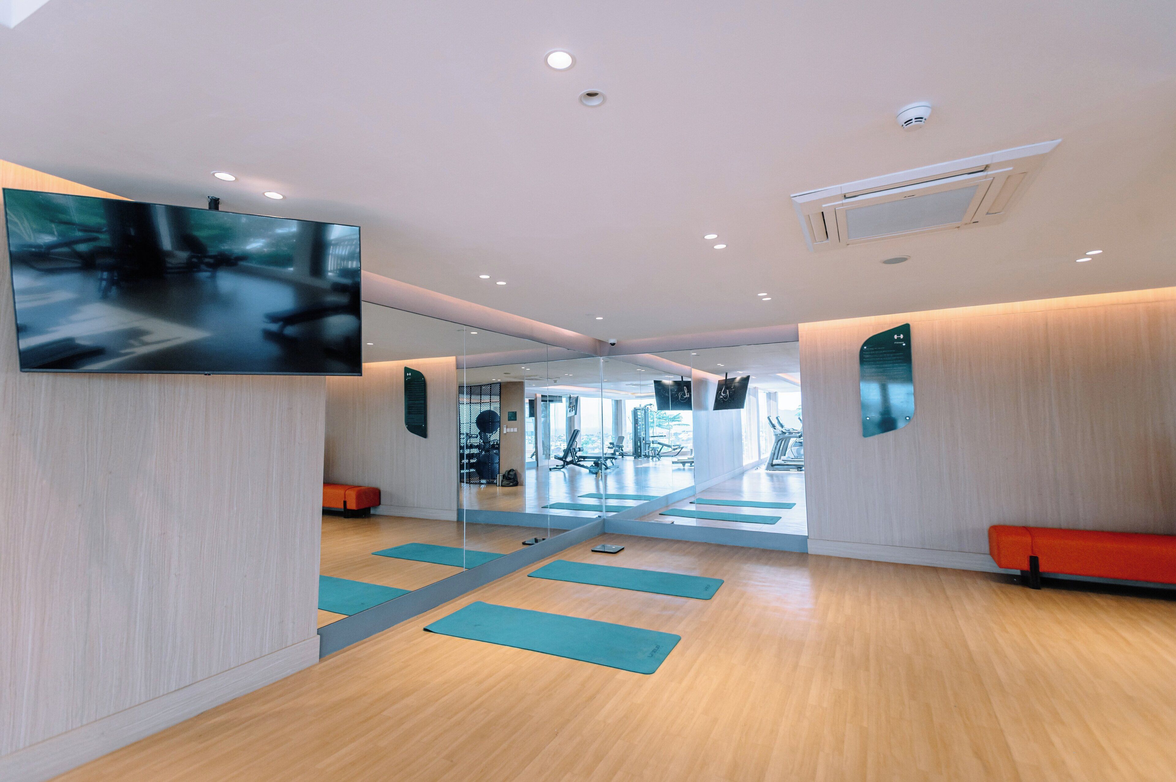 A modern gym with wooden floors, exercise mats, and mirrored walls.
