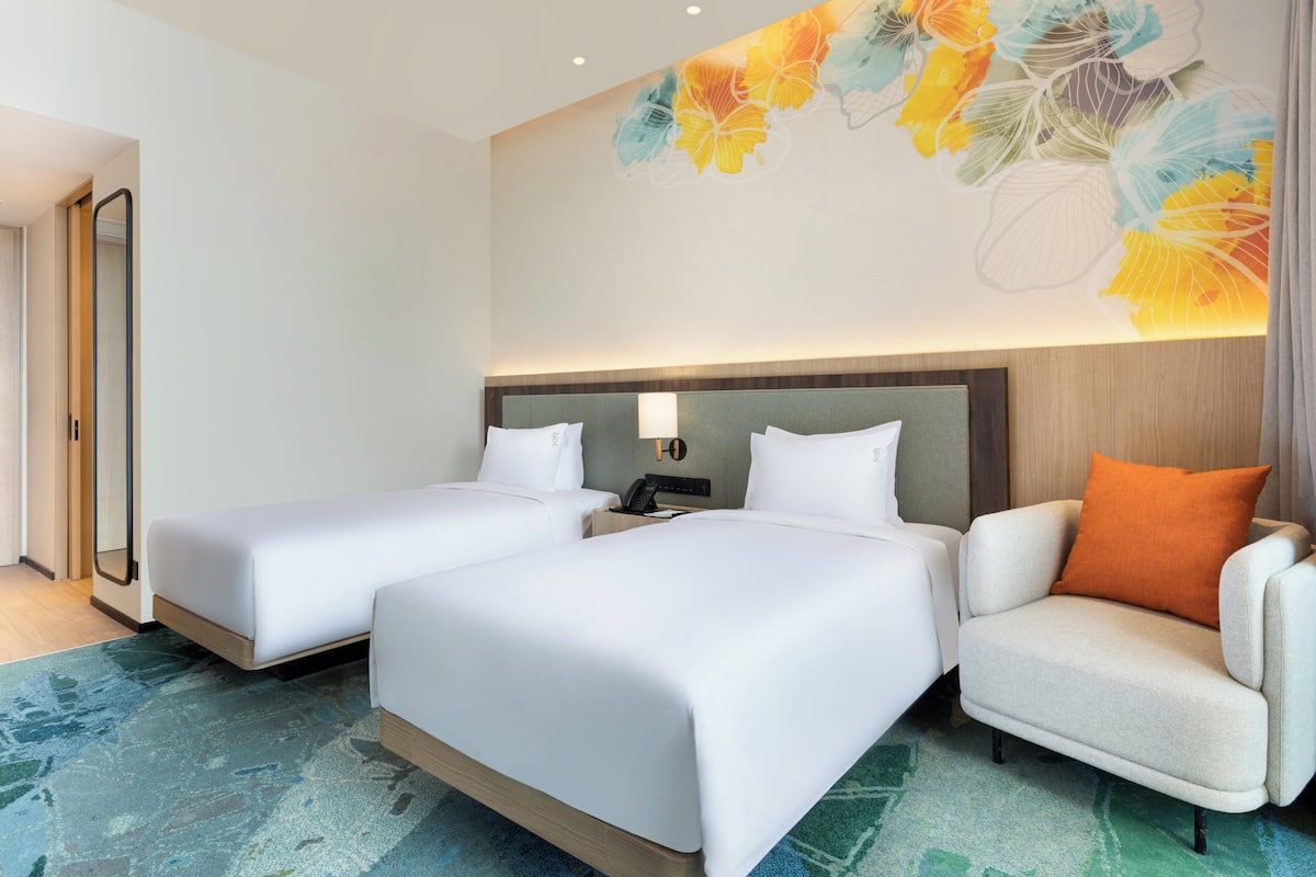 A hotel room with two beds, a nightstand, a lamp, and a chair.