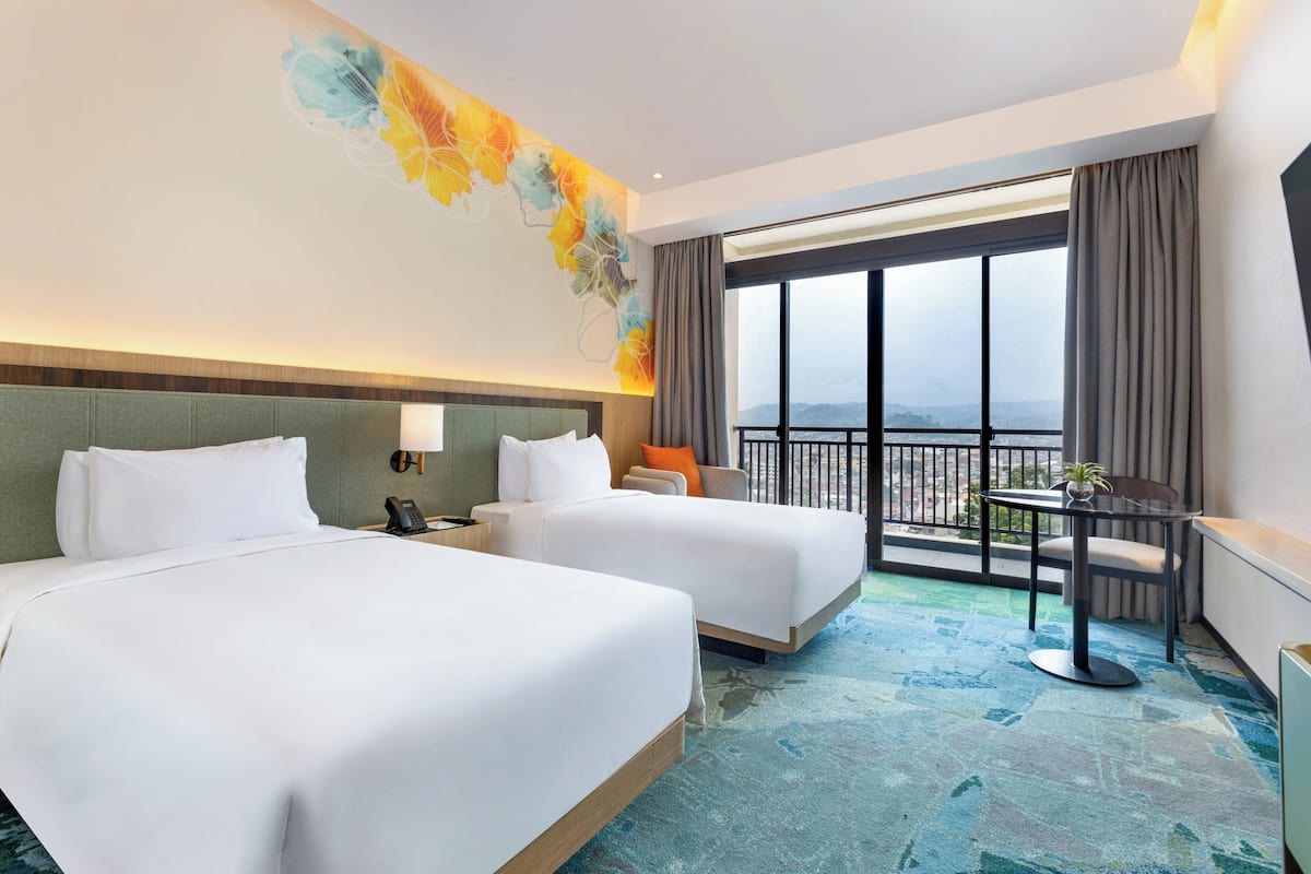 A hotel room with two beds, a balcony with a view, and a small table with a plant.