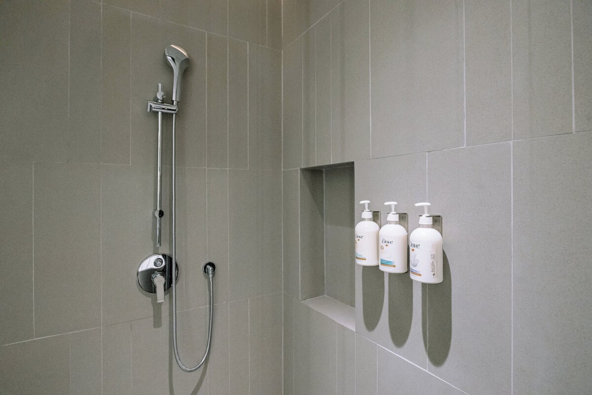 A shower area with a handheld showerhead, a wall-mounted faucet, and a shelf with three bottles of Dove body wash.