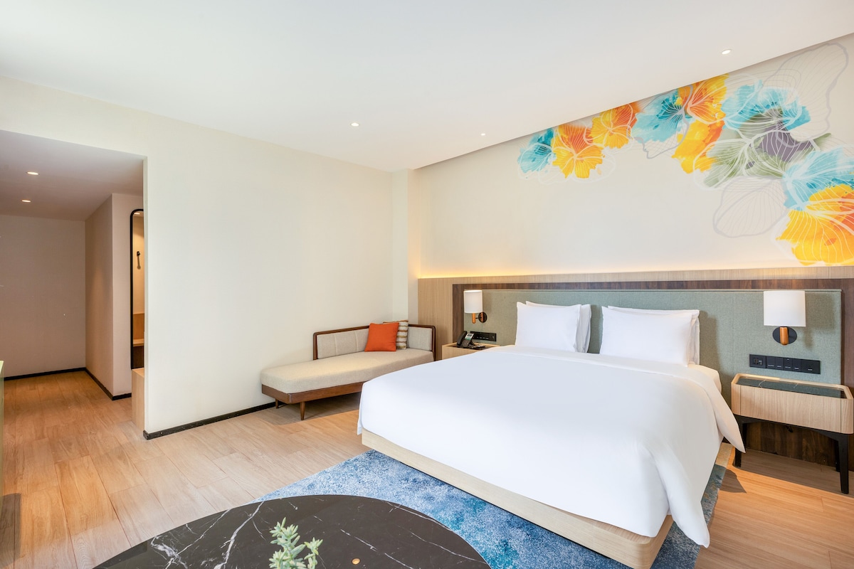 A hotel room with a large bed, a sofa, a nightstand, and a wall with a floral mural.