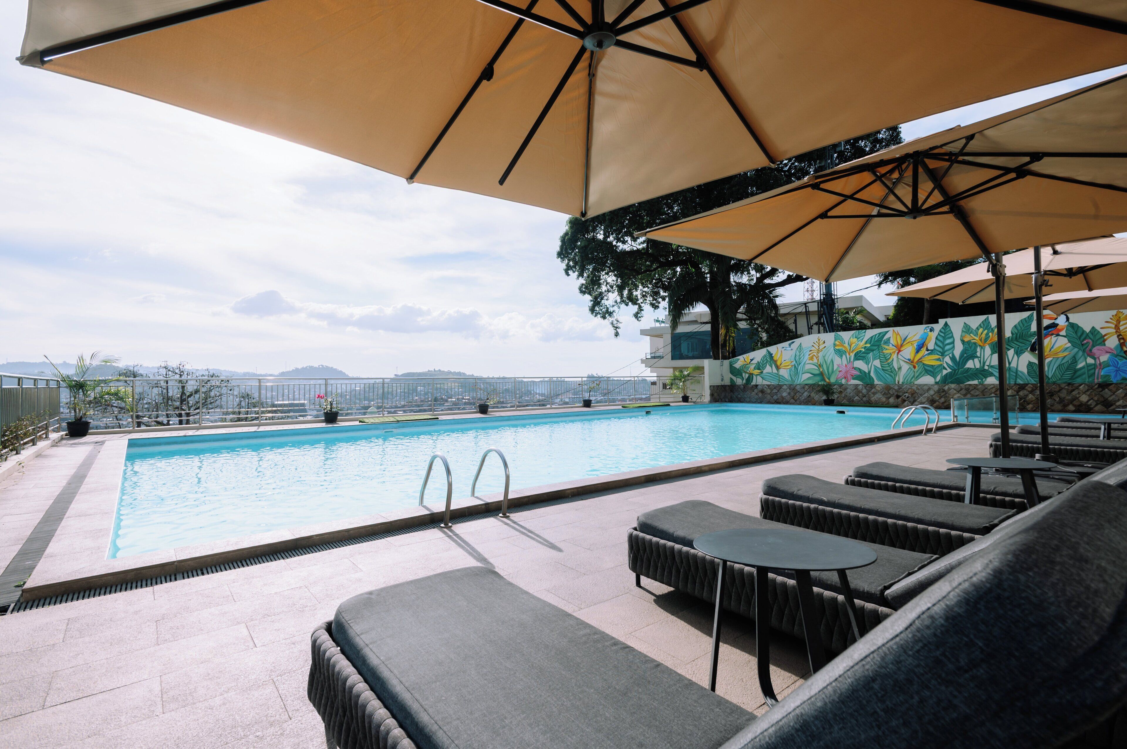 A rooftop pool area with lounge chairs and umbrellas, a view of the cityscape, and a decorative wall.