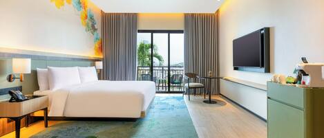 A hotel room with a large bed, a flat-screen TV, a desk with a phone, a small table with chairs, and a view of the outdoors.