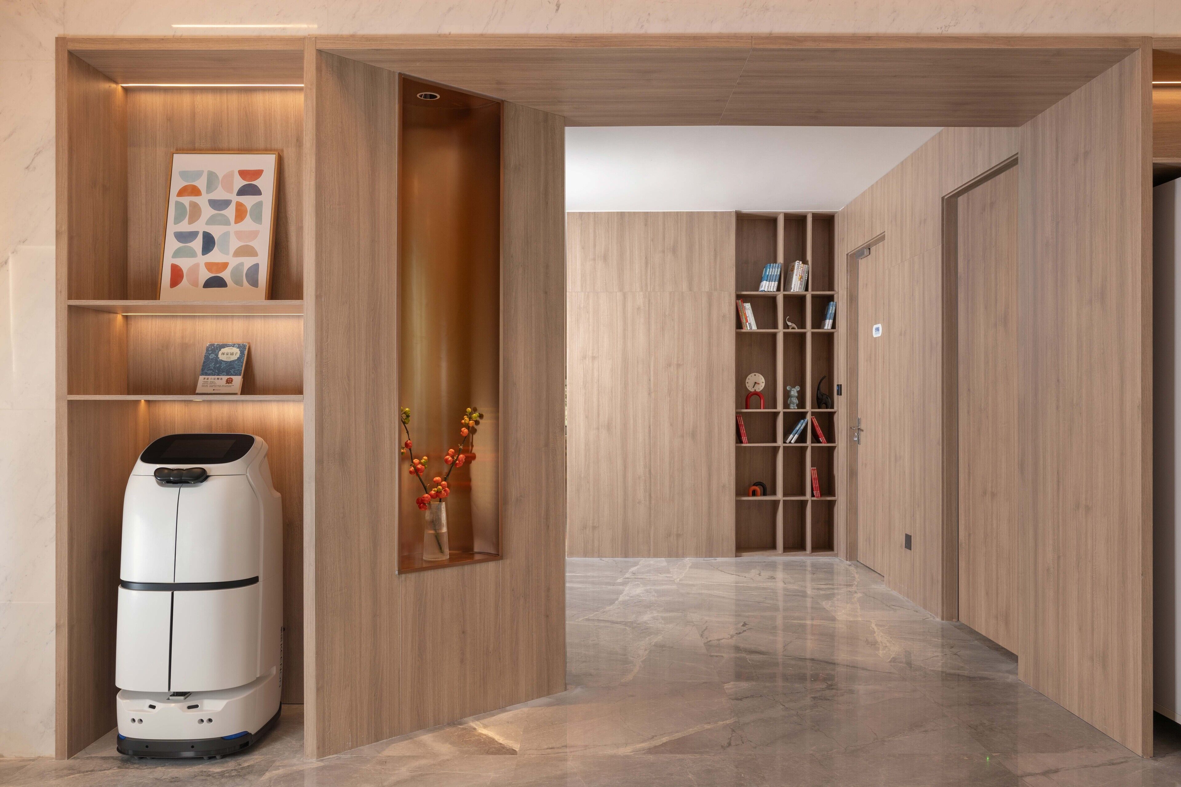 A hallway with wooden paneling, a robotic vacuum cleaner, and a shelf with books and decorative items.