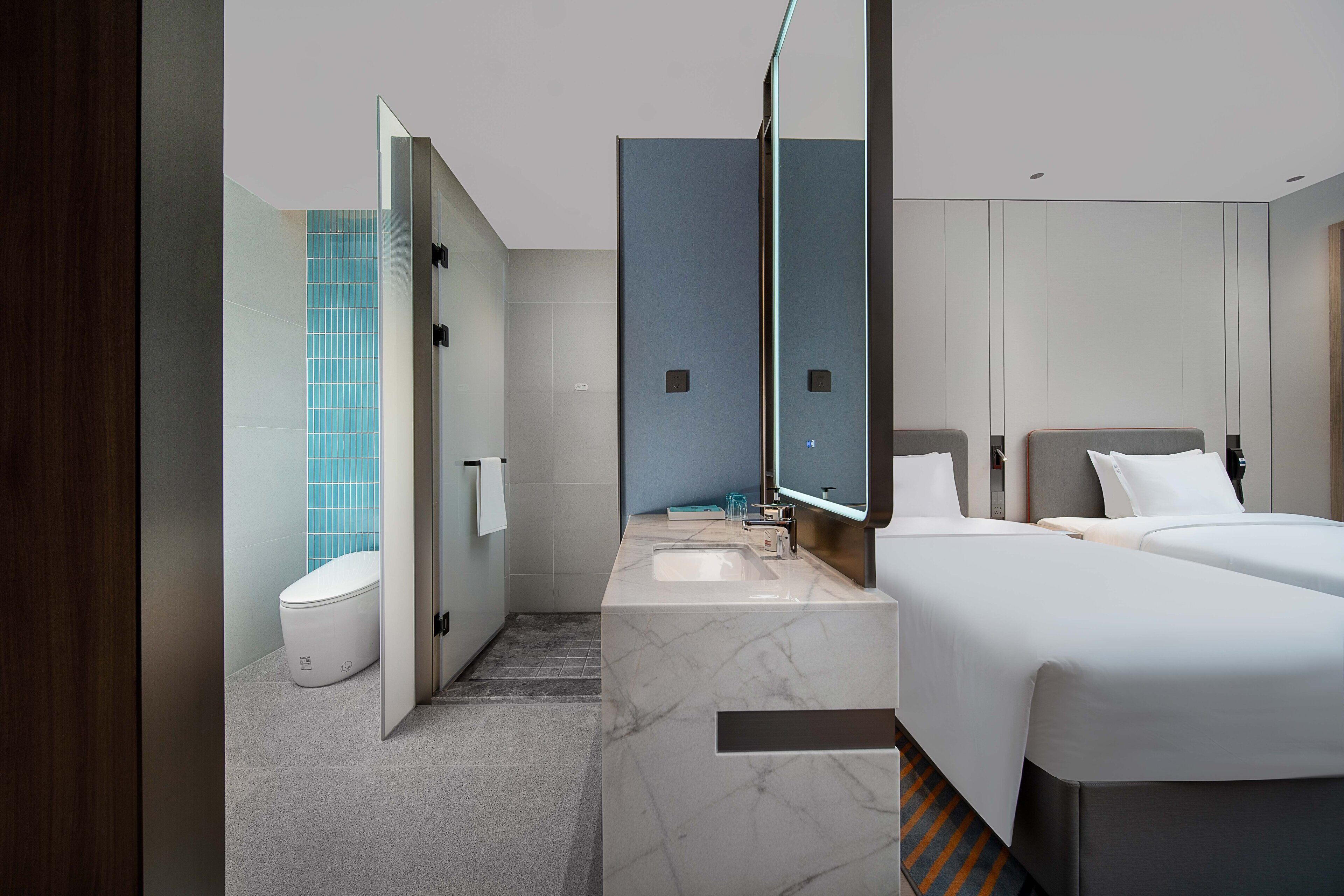 A modern hotel room with a marble bathroom, a large mirror, and a bed with two pillows.