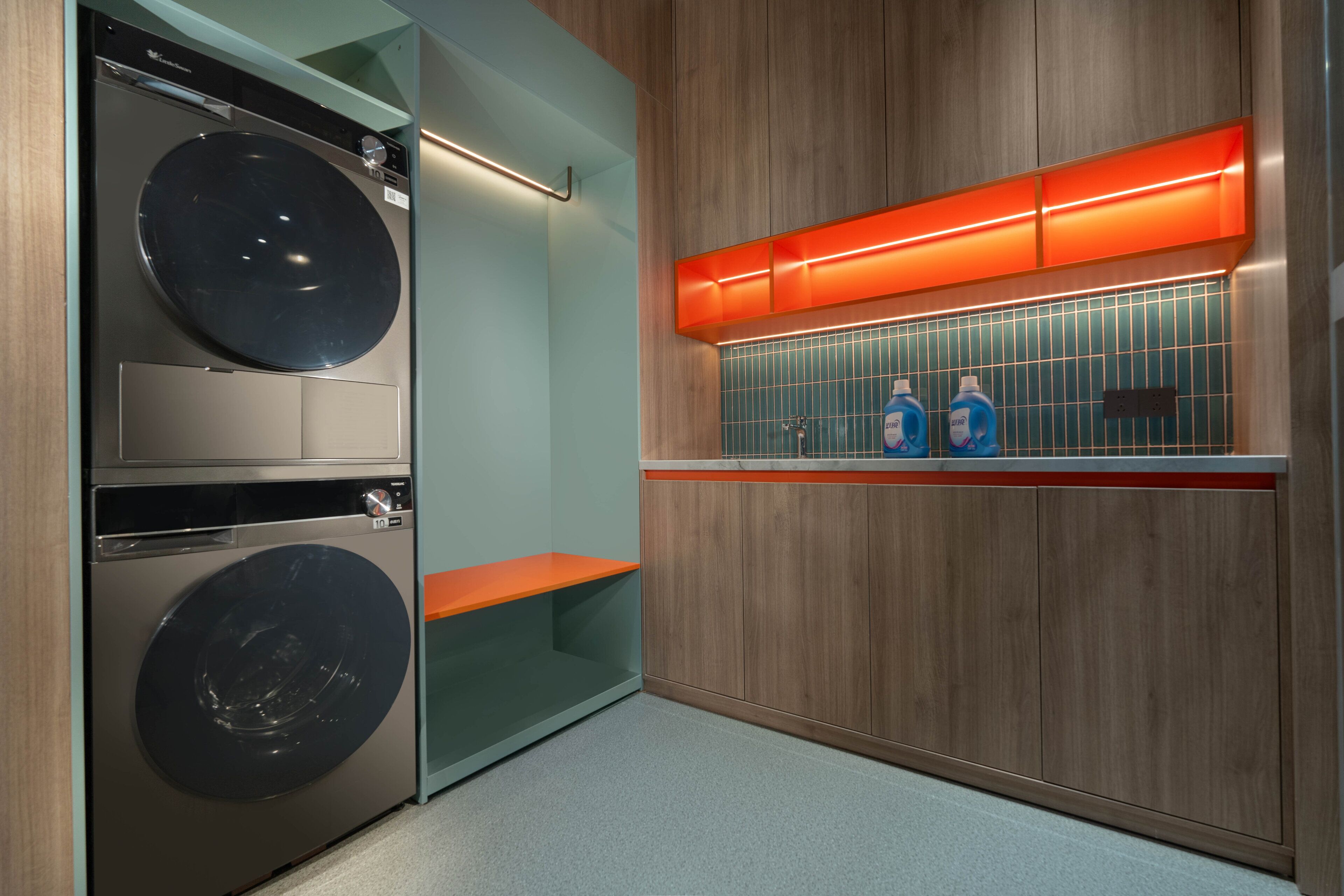 A laundry room with two stacked washing machines, a shelf with bottles, and wooden paneling.