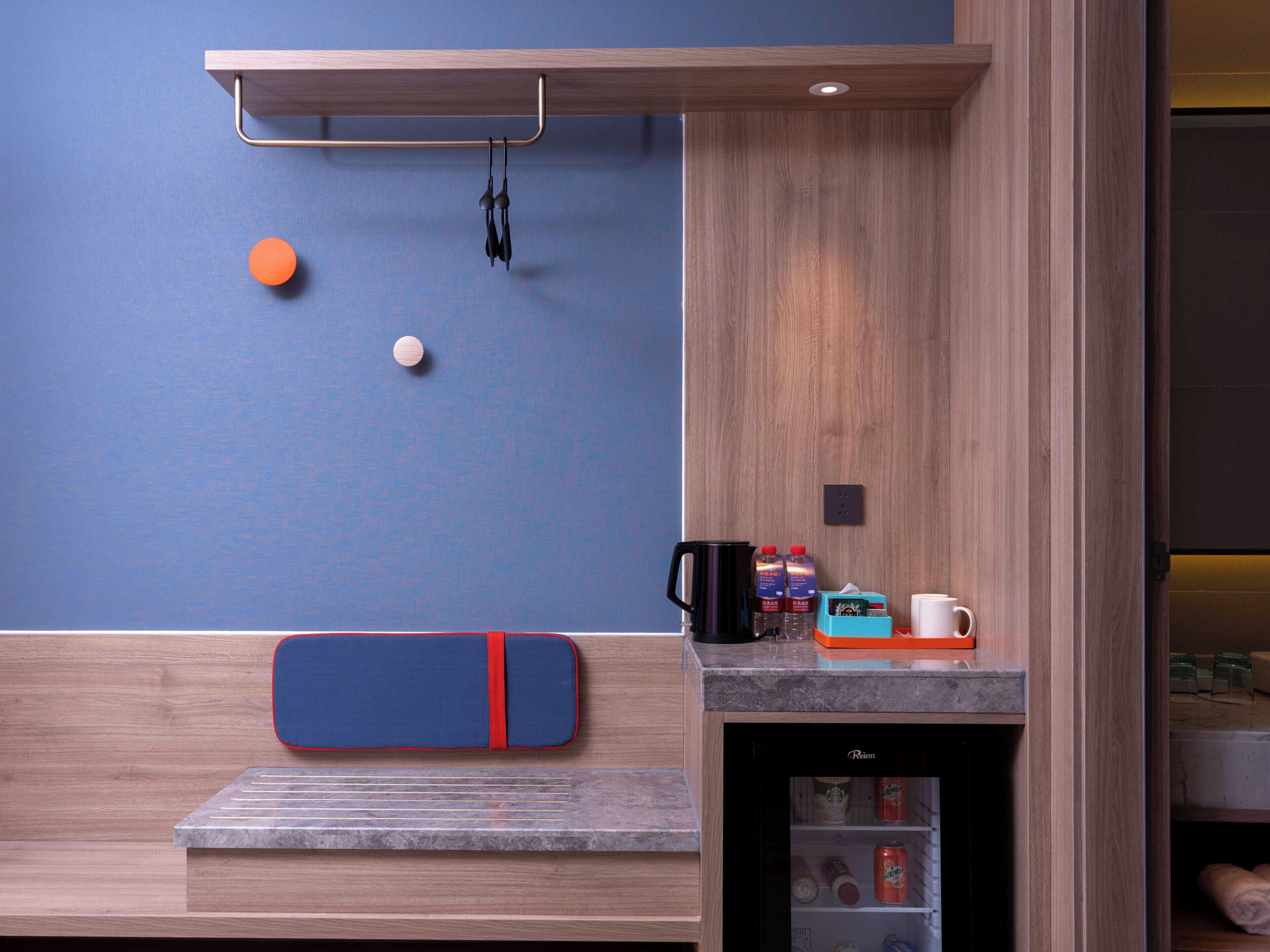 Quarto com um banco de madeira, uma pequena mesa com cafeteira, garrafas e uma geladeira.
