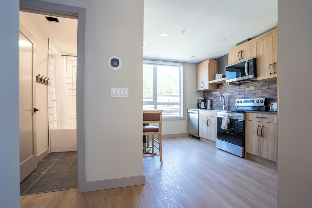 A modern kitchen with wooden cabinets, a built-in microwave, and an oven. There is a window providing natural light and a view of the outdoors.