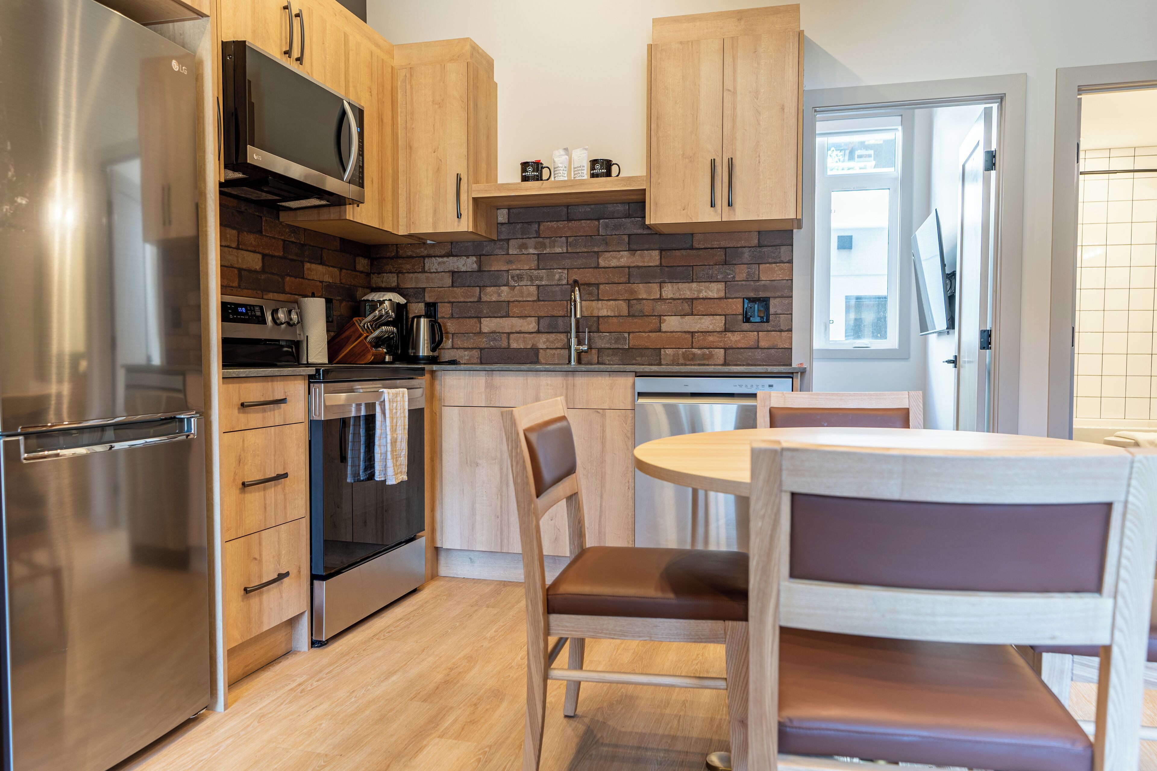 A modern kitchen with wooden cabinets, a stainless steel refrigerator, a microwave, and a brick backsplash.