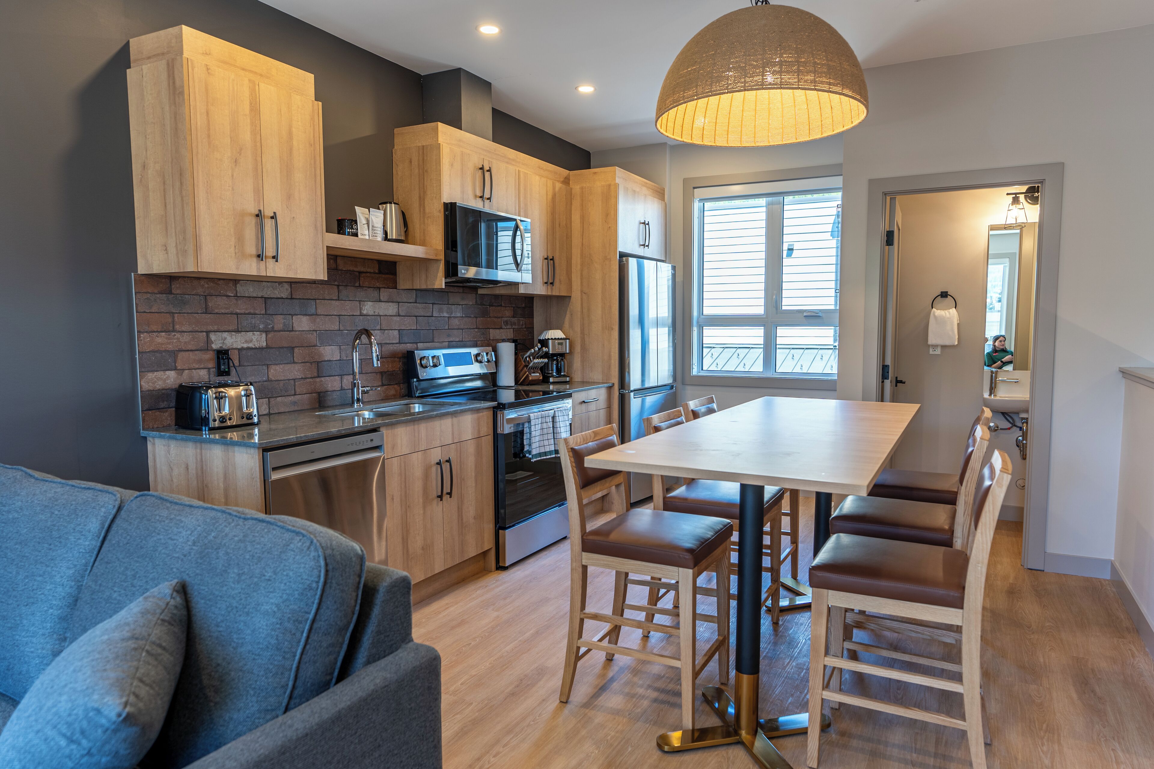 A modern kitchen with wooden cabinets, a brick backsplash, stainless steel appliances, and a dining area with a large table and chairs.