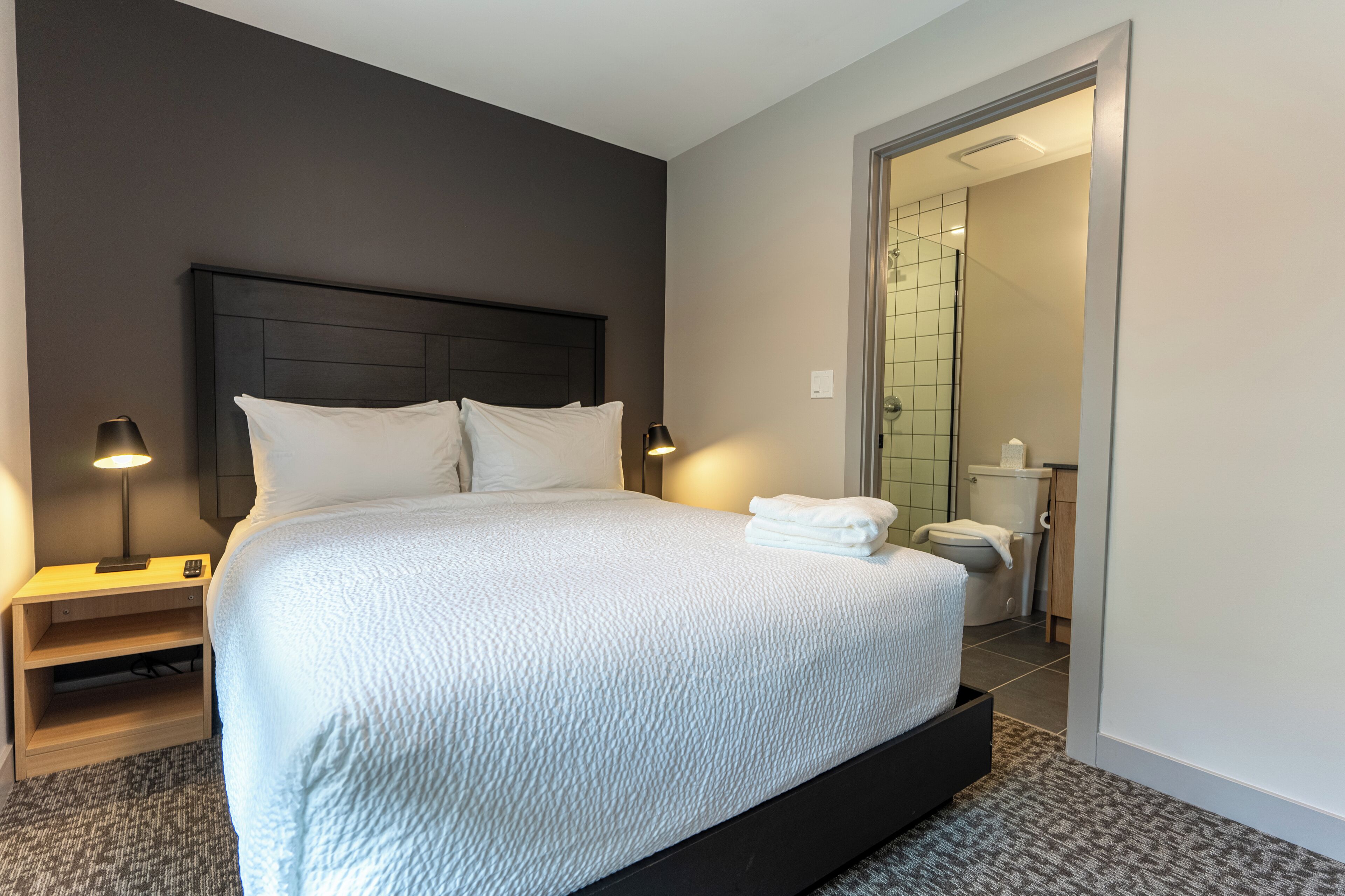 A neatly made bed with white linens, a dark headboard, and two bedside lamps.