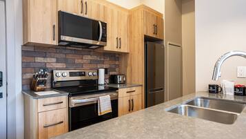 A modern kitchen with wooden cabinets, a stainless steel refrigerator, a microwave, and a granite countertop.