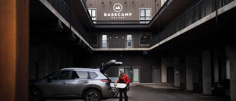 Un parking avec un bâtiment portant l’inscription « BASECAMP SUITES » et une voiture dont le coffre est ouvert.