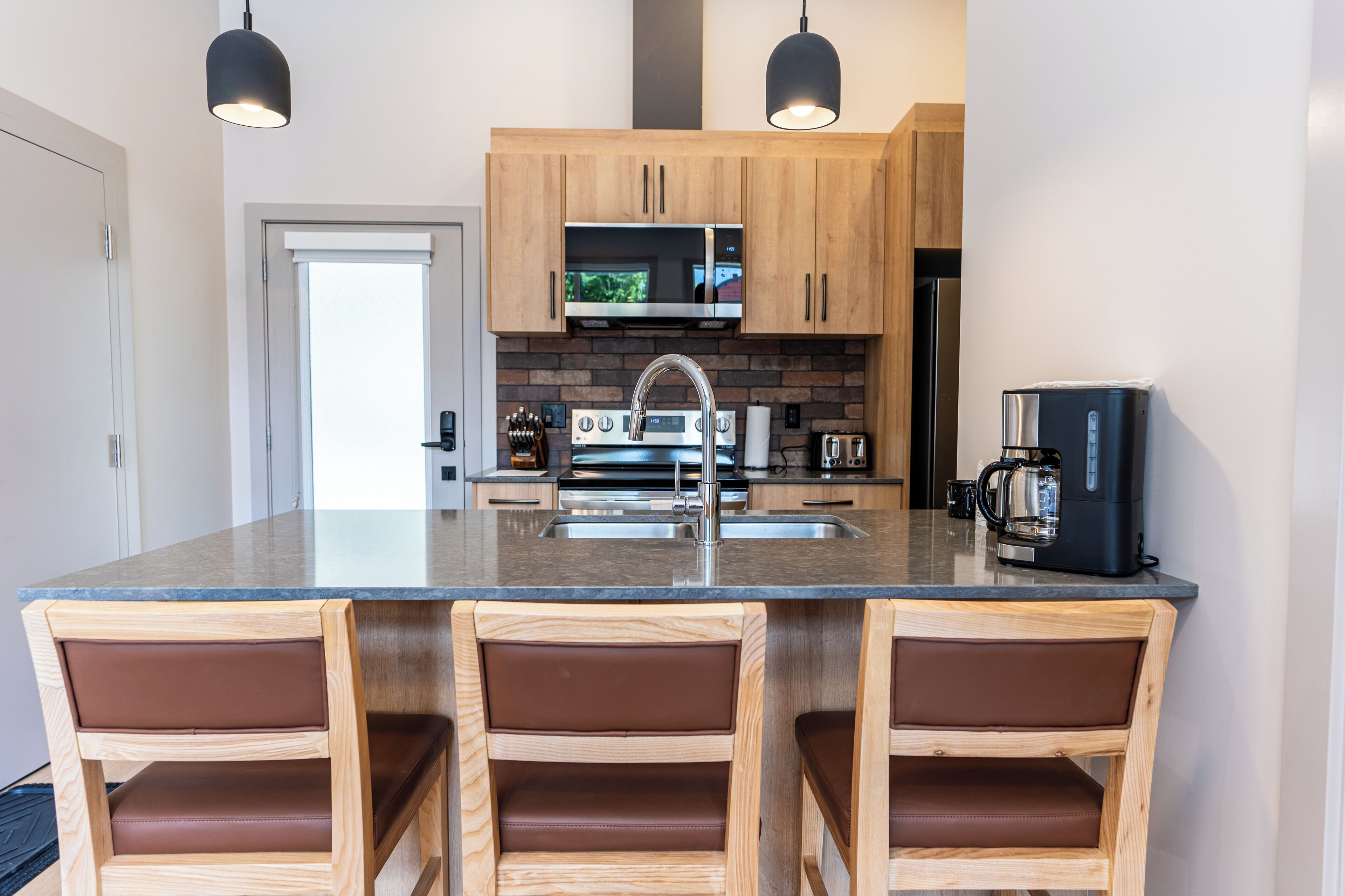A modern kitchen with a central island, wooden cabinets, a microwave, a coffee maker, and a refrigerator.