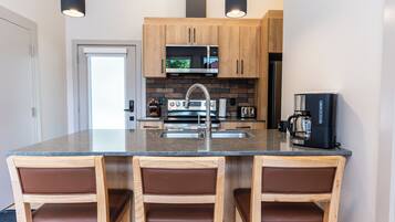 A modern kitchen with a central island, wooden cabinets, a microwave, a coffee maker, and a refrigerator.