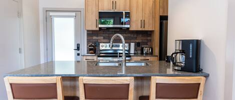 A modern kitchen with a central island, wooden cabinets, a microwave, a coffee maker, and a refrigerator.