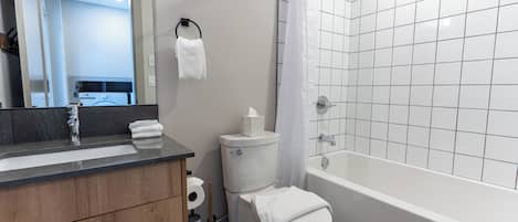 A bathroom with a white toilet, a sink with a mirror, a bathtub, and a shower curtain.