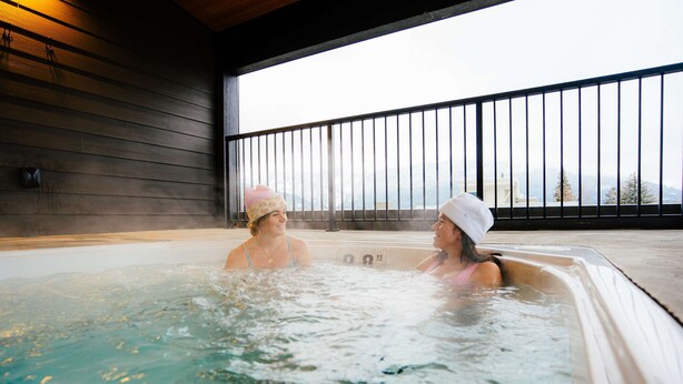 Dos personas en un jacuzzi con una pared de madera y un balcón con barandilla.