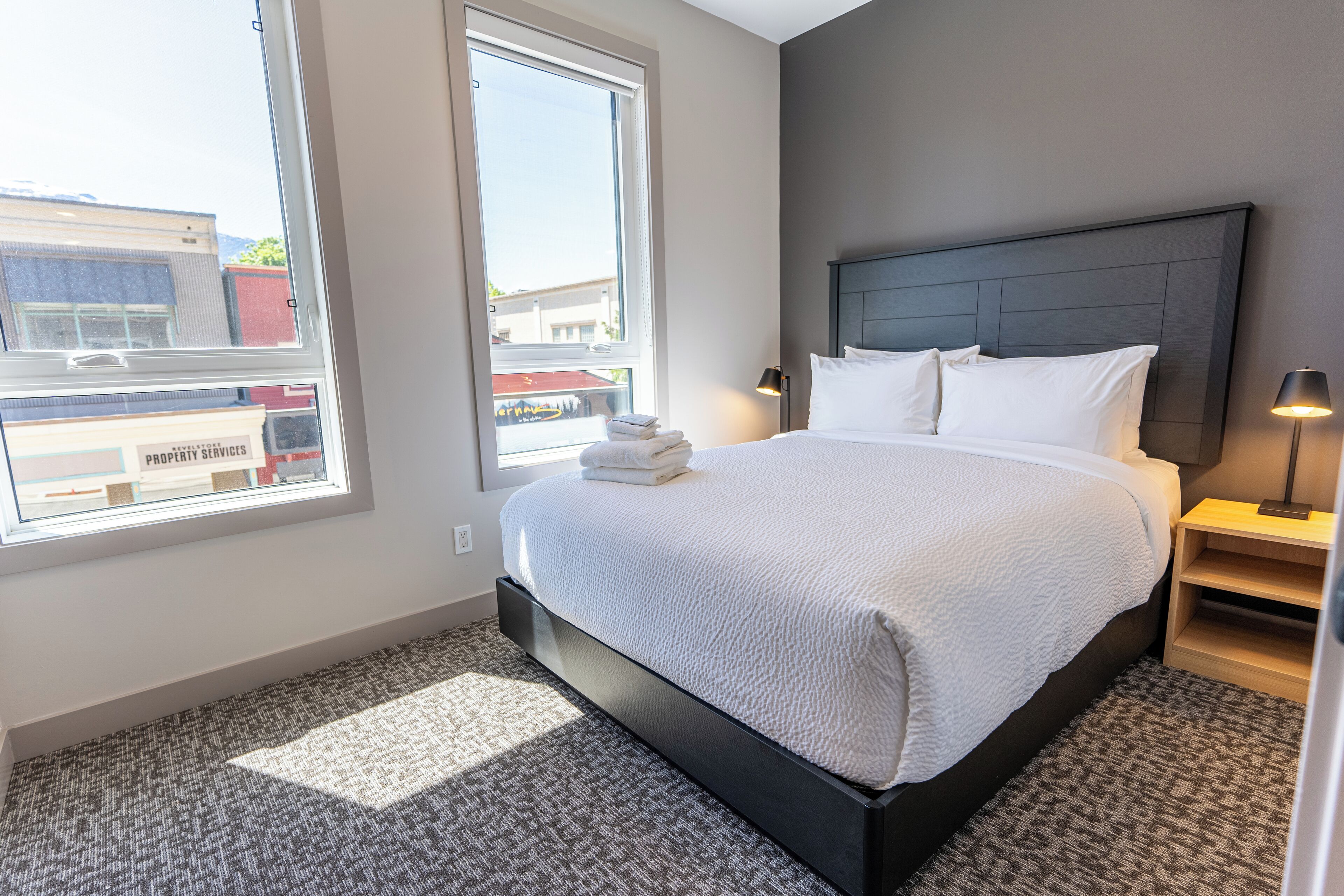 A modern hotel room with a large bed, a nightstand, and a window with a view of the city.