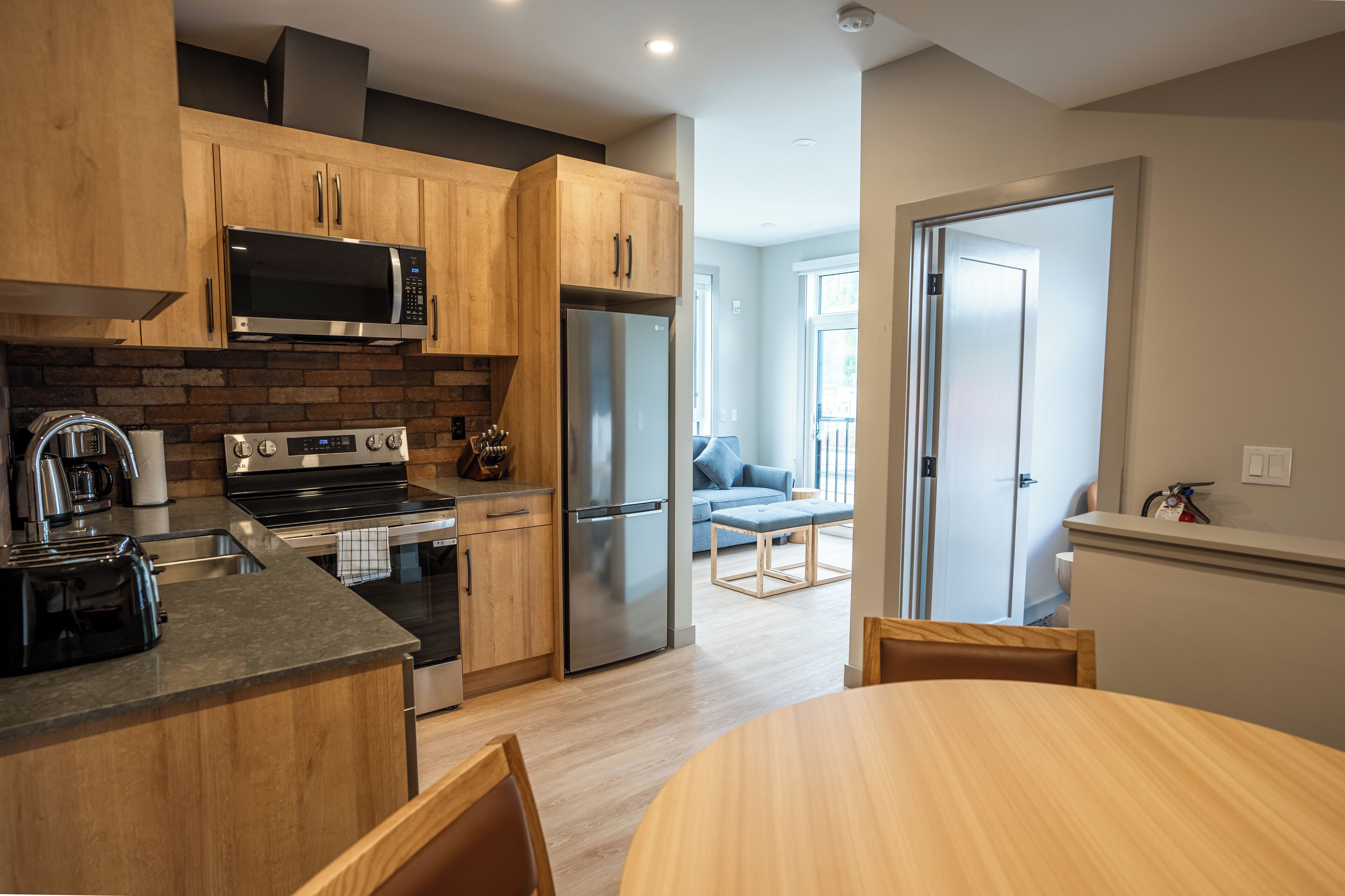 A modern kitchen with wooden cabinets, stainless steel appliances, and a dining area with a wooden table and chairs.
