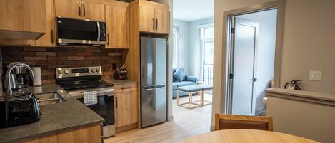 A modern kitchen with wooden cabinets, stainless steel appliances, and a dining area with a wooden table and chairs.