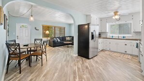 Una cocina moderna con armarios blancos, un refrigerador negro y una zona de comedor con una mesa y sillas de madera.