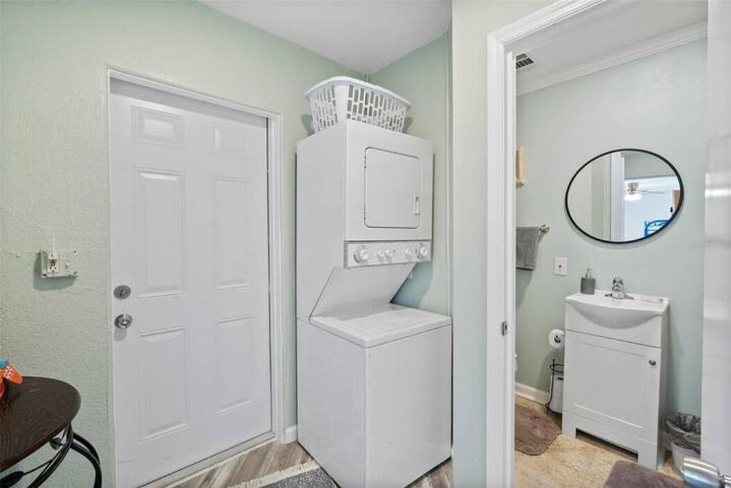 Un lavadero con lavadoras y secadoras apiladas, una puerta blanca y un baño con lavabo y espejo.