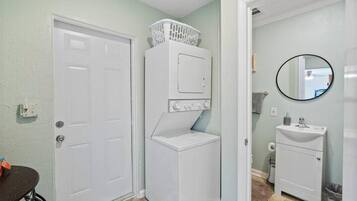 Un lavadero con lavadoras y secadoras apiladas, una puerta blanca y un baño con lavabo y espejo.