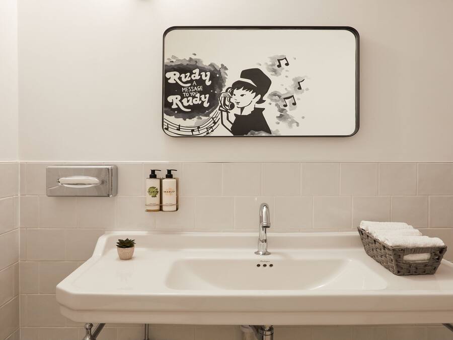 A bathroom with a white sink, a mirror, a framed artwork, a soap dispenser, and a small potted plant.